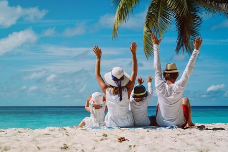 Family of four sitting on the beach with their hands up